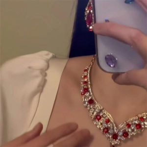 Detail shot of vintage gold necklace and teardrop earrings with red crystals on a model