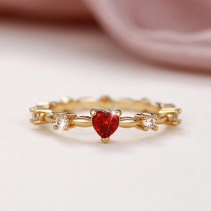 Macro view of gold heart ring with red zircon and sparkling stones on silk background