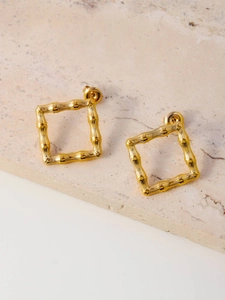 Macro shot of gold square bamboo style earrings on a beige textured stone background