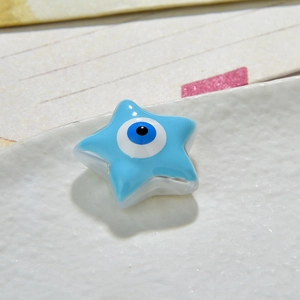 Macro shot of a light blue star-shaped resin evil eye bead on a white textured ceramic dish