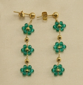 Detailed close-up of long tassel gold earrings with green crystal flowers and beads