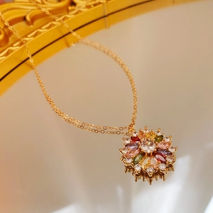 Detail of gold-plated flower pendant with pink and green zircon stones on reflective surface