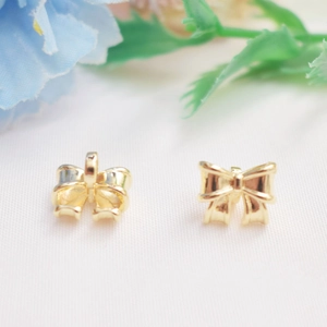 Macro shot of 14K gold-plated bow charm pendants on white fabric for DIY jewelry making