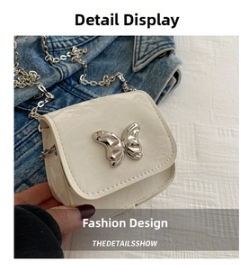 Close-up of a cream patent leather crossbody bag featuring a silver metal butterfly clasp