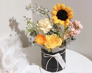 Close-up of a vibrant sunflower and rose bouquet in a black round gift box with a white ribbon