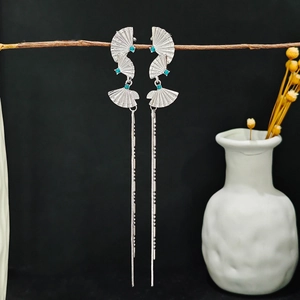 Detailed shot of silver fan-shaped tassel earrings hanging on a dry branch background