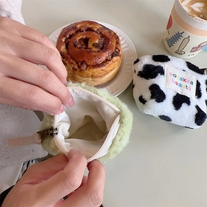 Plush makeup bags in light green and cow print shown in a cozy cafe setting with coffee