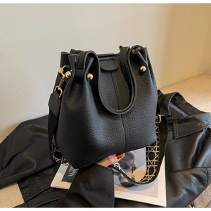 Detail of black lychee grain bucket bag with woven strap and golden hardware accents