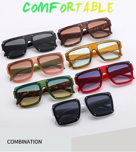 Flat lay of oversized square sunglasses in seven assorted colors with metal rivet details