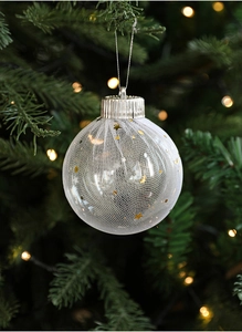 Close-up of a clear Christmas ball with white mesh and gold stars on a tree