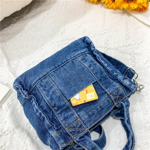 Close-up of dark blue denim tote bag with visible yellow stitching and outer pocket