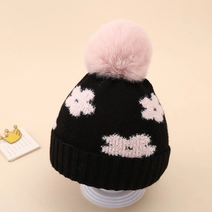 Detail of baby winter knit hat featuring pink floral pattern and large soft pom-pom