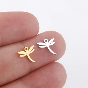 Miniature dragonfly charms in gold and silver steel held on a fingertip for size