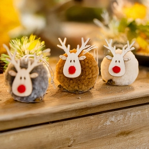Three Christmas reindeer ornaments made of wood and plush balls on a rustic wooden table