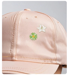 Detailed close-up of daisy and lily enamel pins pinned on a pink satin baseball cap