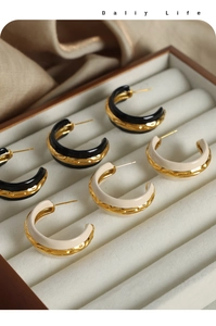 Detail of C-shaped gold plated earrings with enamel finish and hammered texture