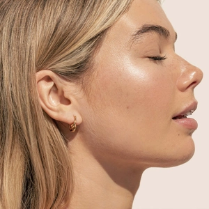 Detail of 18K gold-plated twisted hoop earring worn on model with warm golden finish