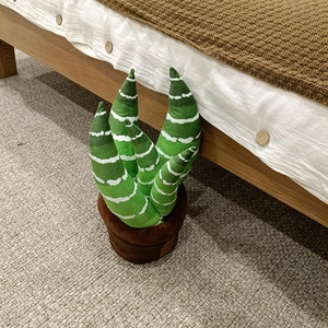 Détail d'une plante en peluche verte aux rayures blanches dans un pot en tissu marron