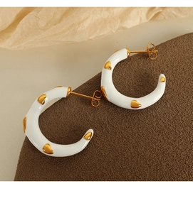 Macro detail of white enamel C-shape stainless steel earrings with gold heart patterns