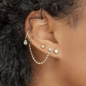 Detail of layered gold earrings set with zircon studs and a delicate tassel chain on ear