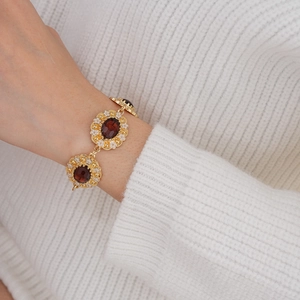 Detail of vintage gold bracelet with red oval gemstones and floral accents on wrist