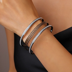 Close-up of multilayer geometric metal bracelets featuring silver and copper textures