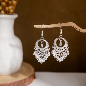 Detail of silver ethnic peacock tassel earrings with hollow leaf design on wood