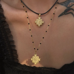 Close-up of layered 18k gold plated St. Benedict medal necklaces on a neck with black cord