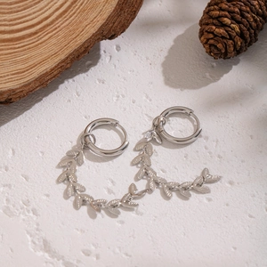 Close-up of silver leaf tassel earrings on wood and pinecone natural background
