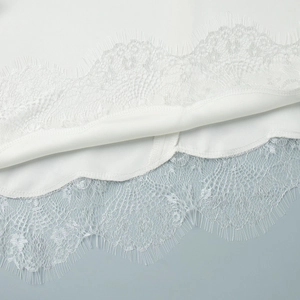 Close-up of white satin fabric with delicate eyelash lace trim and floral embroidery