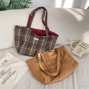Detail of reversible plaid tote bag with suede texture and embroidery on sofa