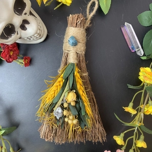 Detailed view of a handmade decorative broom with blue crystal and dried yellow flowers