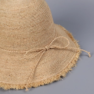 Close-up of hand-woven raffia straw sun hat with fringe brim and bow detail