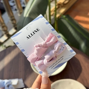 Detail view of two pink twill bow hair clips with stars on an ALLINE card