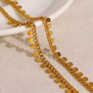 Minimalist gold necklace with circular pendant discs shown on white ceramic plate