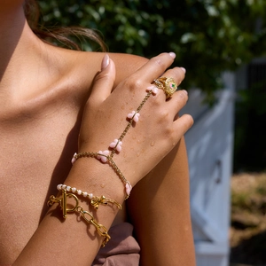Luxury gold flower bracelet and ring set with pink enamel on model's hand with water drops