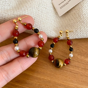 Detail of beaded hoop earrings with tiger eye stone, red agate and pearls on linen