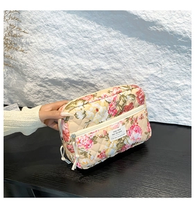 Detail of floral quilted cosmetic bag with zipper and hand-held texture on wood