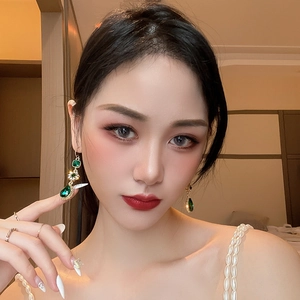 Close-up of vintage emerald teardrop earrings with gold inlay on an elegant model
