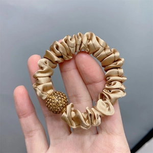 Detail of a golden silk scrunchie with a sparkling rhinestone ball charm in hand
