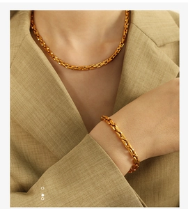 Close-up of a model wearing a gold Cuban link necklace and bracelet set with khaki blazer