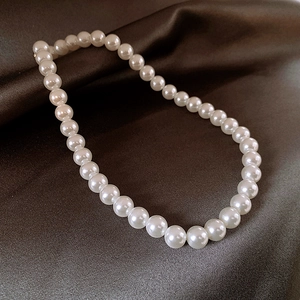 Elegant white pearl necklace with glossy round beads on dark brown satin background