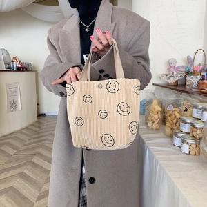 Close-up of beige corduroy tote bag with black smiley faces and metal snap buckle