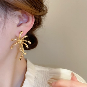 Close-up of model wearing gold flower-shaped earrings with polished metallic abstract lines