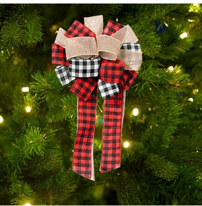 Detail of red and black plaid burlap Christmas bow hanging on a decorated tree with warm lights