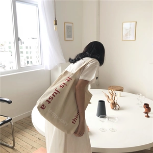 Detail of beige canvas tote bag featuring red typographic print on minimalist fabric
