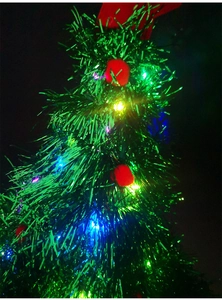 Detail of glowing green Christmas tree hat with red pom-poms and LED lights