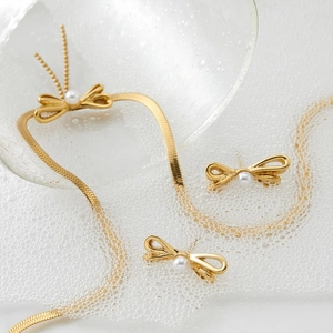 Elegant gold bow necklace and earrings set with pearls on a fresh water-droplet surface