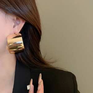 Close-up of golden wide curved C-hoop earring with polished mirror finish on model