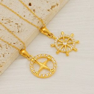 Close-up of gold compass and rudder pendants with sparkling stones on stone background